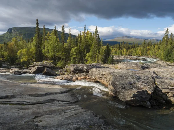 Piękny krajobraz północny z dziką rzeką lodowiec Kamajokk, głazy i świerk lasu w Kvikkjokk w szwedzkiej Laponii. Letni słoneczny dzień, złota godzina, dramatyczne chmury — Zdjęcie stockowe