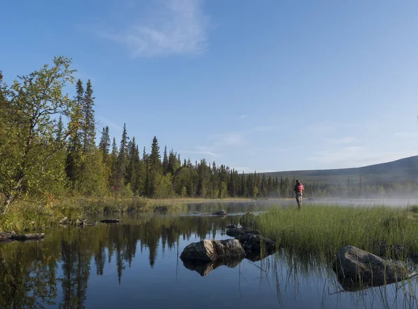 Pescador hombre la captura de peces en el lago Sjabatjakjaure en Hermosa niebla de la mañana soleada niebla en Suecia Laponia naturaleza. Montañas, abedules, bosques de abetos. Cielo azul —  Fotos de Stock