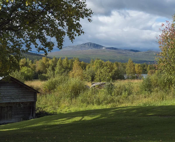Traditionelle Holzhütte mit Blick auf die wunderschöne Landschaft des Sarkgebirges und des Flusses Kamajokk in Kvikkjokk in Schwedisch Lappland. Sommer sonniger Tag, goldene Stunde, dramatische Wolken — Stockfoto