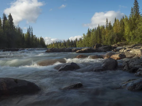Piękny krajobraz północny z długą ekspozycją strumień wody rzeki Kamajokk, głazy i świerk lasu drzewa w Kvikkjokk w szwedzkiej Laponii. Letni słoneczny dzień, złota godzina, dramatyczne chmury — Zdjęcie stockowe