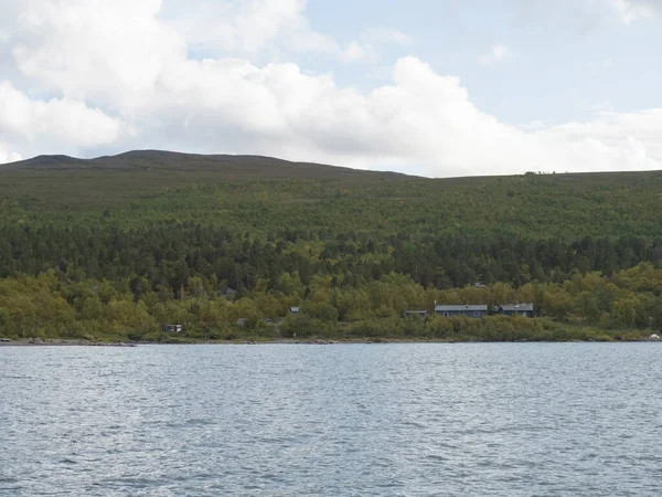 Vista de la cabaña sami en Saltoluokta desde el río Lulealven con montañas verdes, abedul y nubes blancas cielo azul —  Fotos de Stock
