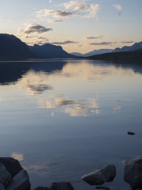 İsveç Laponya, Saltoluokta 'daki Lulealven Gölü üzerinde güzel mavi turuncu gün batımı. Dağların yansıması, bulutlar ve gökyüzü suyu temizliyor. Minimalist, boşluğu kopyala