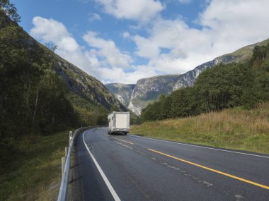 Norveç 'in Romsdal Vadisi' ndeki Trol Duvarı Trollveggen ile birlikte Winding Yolu E136 'daki beyaz karavan vagonu. Mavi gökyüzü beyaz bulutlar. Yaz gezisi manzarası.