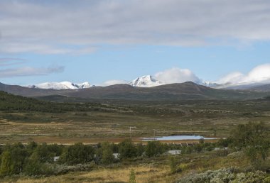 Tepelerde sonbahar manzarası ve kar kaplı dağlar Dovre Nasjonaalpark doğa parkında E6, Norveç 'ten dramatik bulutlarla kaplı.