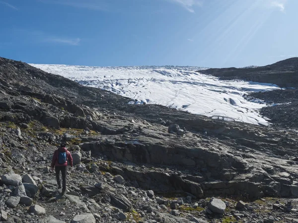 Homme randonneur en duvet rouge sur le sentier de randonnée au glacier Smorstabbreen dans le parc national de Jotunheimen, Norvège. Journée ensoleillée, fond bleu ciel — Photo