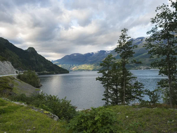 Uitzicht over het blauwe water van Hardanger Fjord in Kinsarvik in Noorwegen met klein dorpje aan de kust. Natuur en reisachtergrond. Vroege herfst gouden uur licht. — Stockfoto