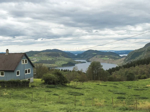 Niebieski drewniany dom z widokiem na fiord boknafjord, las i bujną zieloną trawę. Norwegia Wczesna jesień, humorzaste niebo — Zdjęcie stockowe