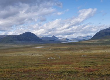Lulealven nehri ile Laponya manzarası, İsveç 'in Saltoluokta yakınlarındaki Kungsleden yürüyüş parkurunda karla kaplı dağ. Sonbahar renkli çalıları, huş ağaçları ve çalıları olan vahşi doğa. Mavi gökyüzü beyaz bulutlar.