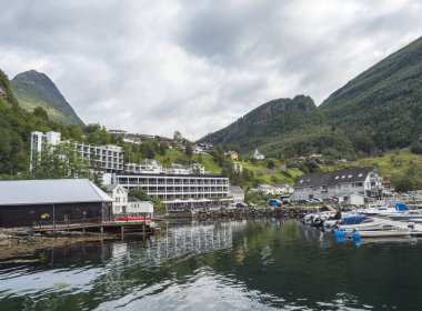 Geiranger, Norveç, 7 Eylül 2019: Geiranger turist köyü limanında küçük tekneleri, oteli ve limanı olan bir manzara. Yeşil kayalıkları, ormanı ve suyu olan Geirangerfjord. erken sonbahar bulutlu günü