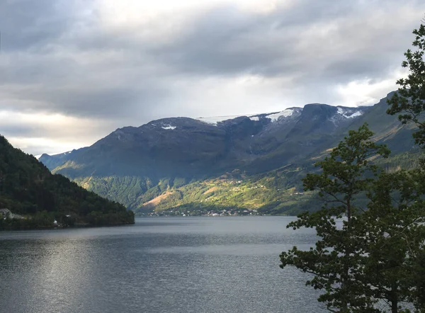 Norveç 'in Kinsarvik kentindeki Hardanger Fjord' un mavi sularının kıyısında küçük bir köye bakın. Doğa ve seyahat geçmişi. Sonbaharın başlarında altın saat ışığı. — Stok fotoğraf