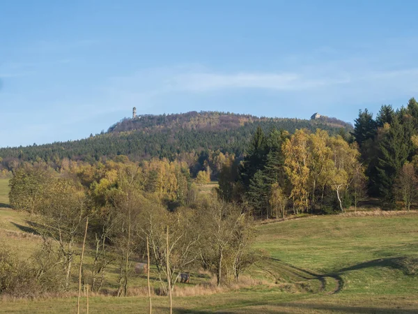 Wiese mit herbstlich bunten Wäldern und Bäumen und Hügeln mit Aussichtsturm und blauer Himmelslandschaft im Lausitzer Gebirge. — Stockfoto