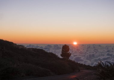 Beyaz bulutların üzerinde güzel kırmızı günbatımı güneş ışınları ve asfalt yollarla kaplı La Palma, Kanarya Adası, İspanya