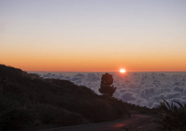 Belo pôr do sol vermelho acima de nuvens brancas cobrir com raios de sol e estrada de asfalto em montanhas em La Palma, Ilha Canária, Espanha — Fotografia de Stock