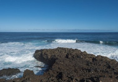 Volkanik kaya oluşumu, kayalık sahilde kayalık lav kayalıkları Atlantik Okyanusu üzerinde beyaz dalgaların ezilmesi. Mavi gökyüzü arka planı. La Palma, Kanarya Adaları.