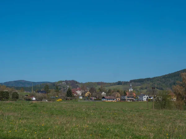 Paesaggio primaverile con vista sul villaggio Cvikov nelle montagne lusiziane con vecchie e moderne case e lussureggiante prato di erba verde, foresta di latifoglie e abeti rossi e colline, sfondo cielo blu — Foto Stock