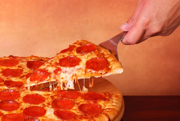 Hand taking a slice of Pepperoni Pizza Stock Photo