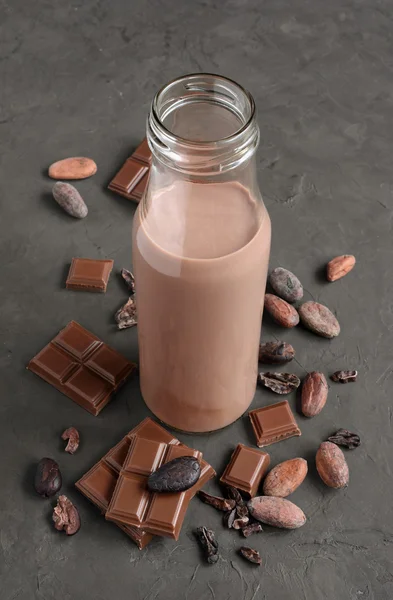 Chocolade melk in een glazen fles met stukjes chocolade bar en cacao bonen — Stockfoto