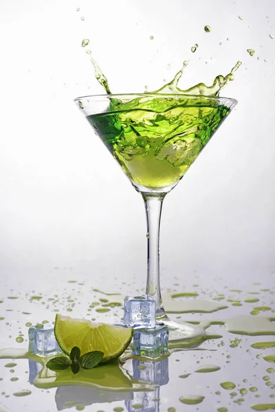 Stänkskydd i glas grön cocktail alkoholdryck med lime, mynta och is kub — Stockfoto