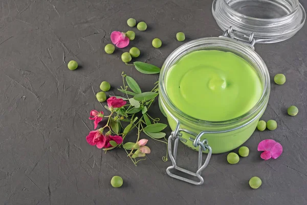 Cibo sano. Purea fresca di piselli verdi in vaso di vetro aperto con fiori rosa di pisello dolce — Foto Stock