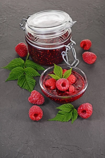 Close up view jam in glass jar and bowl with fresh ripe raspberry and leaves — Stock Photo, Image