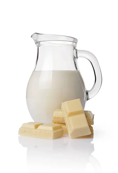 Close-up piece of white chocolate bar with glass jug of milk — Stock Photo, Image