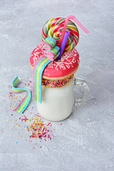 Crazy milk shake with pink donut, color candy and lollipop in glass jar — Stock Photo, Image