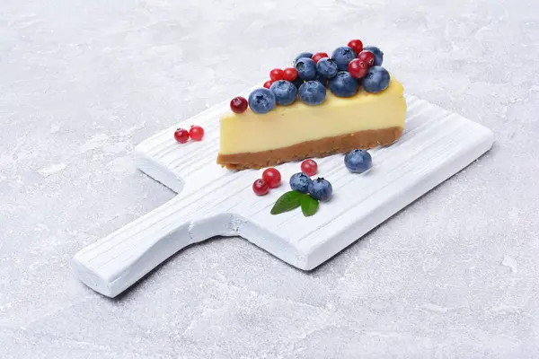 Close-up slice of delicious homemade cheesecake with fresh blueberries and cranberries on white wooden cutting board — Stock Photo, Image