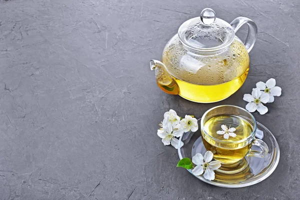 Glass teapot and teacup with green tea and spring flowers — Stock Photo, Image