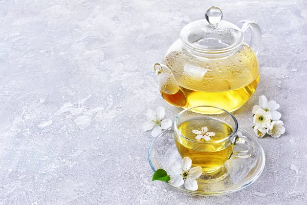 Tetera de vidrio y taza de té con té verde y flores de primavera — Foto de Stock