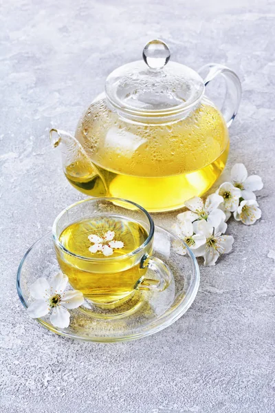 Tetera de vidrio de primer plano y taza de té con té verde y flores de primavera — Foto de Stock
