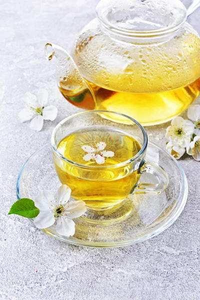 Close-up glass teapot and teacup with green tea and spring flowers — Stock Photo, Image