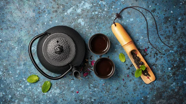 Black japanese cast iron teapot and dry tea in bamboo scoop with mint — Stock Photo, Image