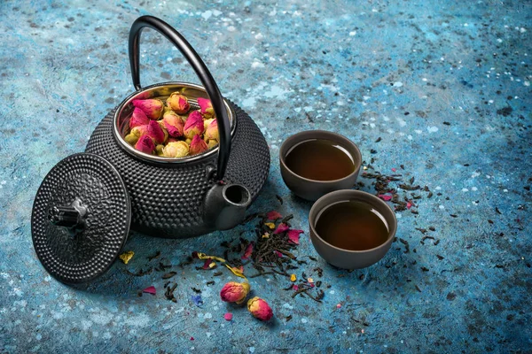 Svart japansk gjutjärn tekanna med te och torra rosor — Stockfoto
