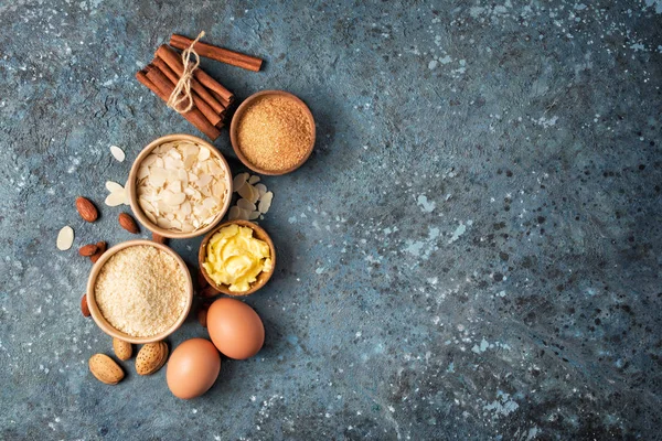 Top view of almond flour and cane sugar in bowls with eggs as ingredient for confectionery on wooden tray and blue concrete background with copy space