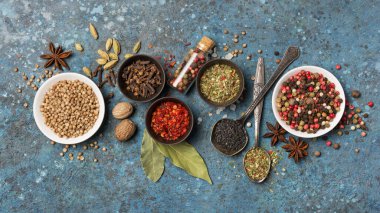 Mavi beton arka planda sağlıklı yiyecekler için malzeme olarak küçük kaseler ve şişelerde bulunan parlak baharat ve otların üst görüntüsü