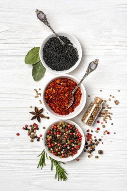 Beyaz ahşap arka planda sağlıklı yiyecekler için malzeme olarak küçük kâseler ve şişelerde bulunan parlak baharat ve otların üst görüntüsü