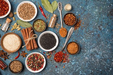 Mavi beton arka planda sağlıklı yiyecekler için malzeme olarak küçük kaseler ve şişelerde bulunan parlak baharat ve otların üst görüntüsü