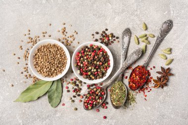 Kaliteli gümüş kaşıklar ve kâselerdeki parlak baharatları gri beton arka planda sağlıklı yiyecekler olarak karıştırmanın en iyi yolu.
