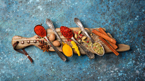 Top view of mix bright spices as ingredient for healthy food on wooden board and blue concrete background