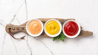Sarı hardal, kırmızı ketçap ve kırmızı biber sosu beyaz mermer arka planda küçük kaseler halinde.