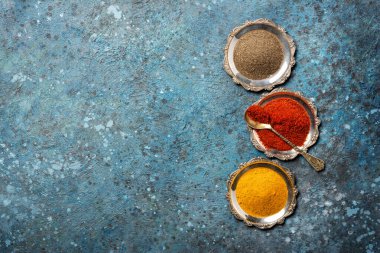 Gümüş tabaklar içindeki parlak zemin baharatlı yemek kaşığıyla mavi beton arka planda fotokopi alanı olan parlak zemin baharatlarının en üst görüntüsü