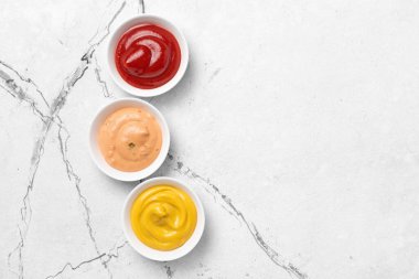 Sarı hardal, kırmızı ketçap ve kırmızı biber sosu beyaz mermer arka planda küçük kaselerde fotokopi alanı ile birlikte.