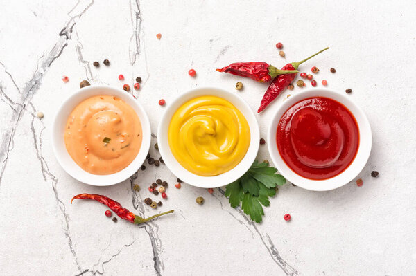 Вид сверху желтой горчицы, красного кетчупа и соуса папаша в маленьких мисках на белом мраморном фоне
