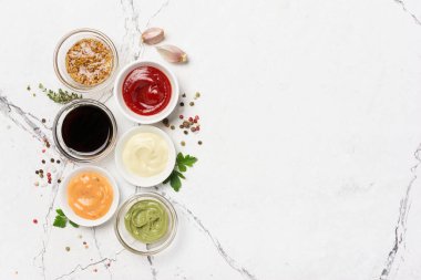 Mayonez, kırmızı ketçap, sarı hardal, yeşil wasabi ve siyah soya soslu beyaz mermer arka planda fotokopi alanı olan kâselerin üst görüntüsü.