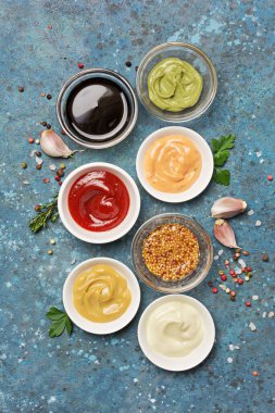 Beyaz mayonez, kırmızı ketçap, sarı hardal, yeşil wasabi ve mavi beton arka planda siyah soya soslu kase manzarası.