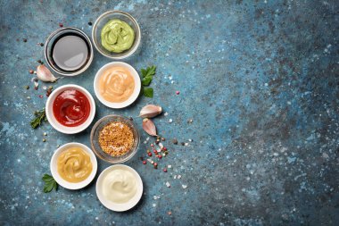 Beyaz mayonez, kırmızı ketçap, sarı hardal, yeşil wasabi ve mavi beton zemin üzerinde siyah soya sosu olan kaselerin üst görüntüsü.