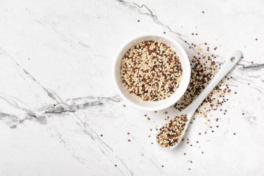 Kinoa tanelerinin üst görünümü beyaz kasede, ışık mermer arka planda, fotokopi alanı ile sağlıklı beslenme gıdası olarak karıştırılır.