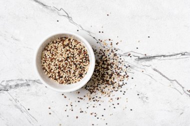 Kinoa tanelerinin üst görüntüsü beyaz kasede hafif mermer arka planda sağlıklı beslenme gıdası olarak karıştırılır