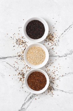 Beyaz kâselerdeki kinoa tanelerinin üst görüntüsü hafif mermer arka planda sağlıklı beslenme gıdası olarak gösterilir.