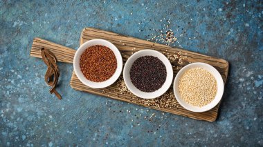 Beyaz kâselerdeki kinoa tanelerinin en üst görüntüsü ahşap tahtada sağlıklı beslenme gıdası ve mavi beton arka plan.